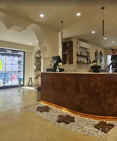 Le comptoir du café, un bloc courbe en cuivre oxydé souligné d'une bande de lumière chaude, derrière des galets blancs incrustés d'empreintes de pattes en bois.